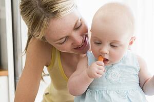 Mother and baby in kitchen eating carrot