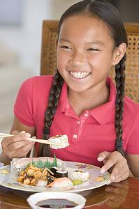 Young girl in dining room eating Chinese food smiling
