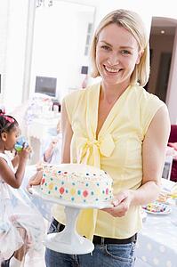 Woman at party holding birthday cake smiling
