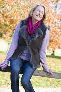 Woman outdoors at park sitting on fence smiling (selective focus)