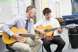 Male student receiving guitar lesson from teacher in classroom