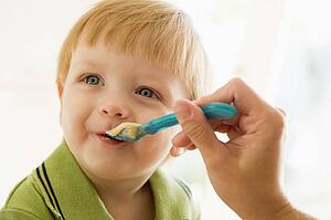 Mother feeding young boy baby food