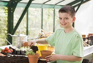 Young boy in greenhouse putting soil in pot smiling