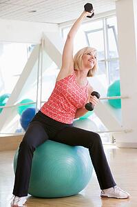 Woman Using Hand Weights On Swiss Ball At Gym
