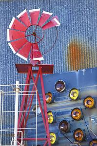 Broken red windmill against rusted blue corrugated metal building covered in taillights