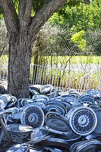 Pile of old hubcaps on the ground next to tree