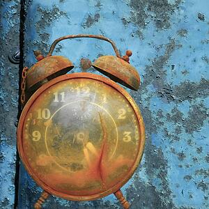 Old weathered alarm clock against rusty blue metal background