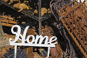 Metal garden decoration of word Home next to rusted metal objects