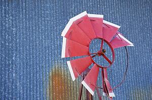 Old red broken windmill against rusted blue corrugated metal building.