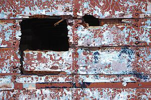 Side of wall with hole and peeling paint.