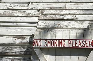Sign on old white peeling building reading 'No smoking please! '.