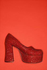 Red glitter high heel shoe against red background.