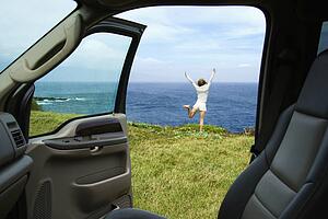 Excited woman standing on grassy cliff by Pacific Ocean in Maui, Hawaii.