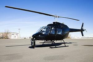 Black helicopter with camera mounted on front parked at airport tarmac.