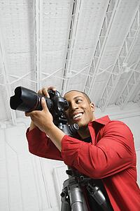 Young male looking through camera on tripod