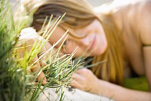 Selective focus portrait of young redheaded woman lying in grass looking at viewer.