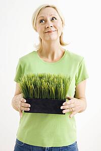 Portrait of woman holding pot of grass and looking up
