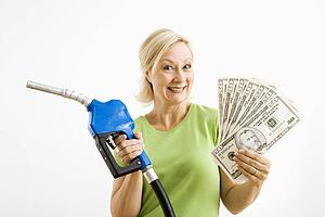 Portrait of smiling adult blonde woman holding gas nozzle and lots of money