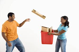 Female holding recycling bin while male tosses cardboard into it