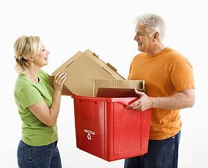 Man holding recycling bin while woman places cardboard into it
