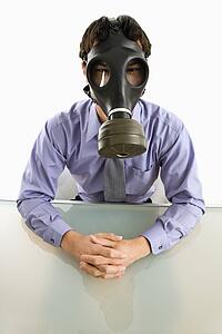 Businessman sitting in white room wearing gas mask