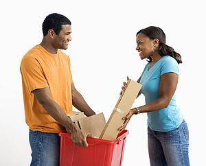 African American male holding recycling bin while pretty female puts cardboard in.