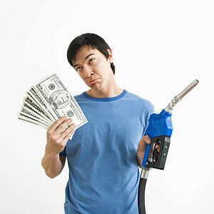 Asian young man with sad expression holding money and gas pump nozzle.