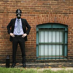 Businessman standing next to brick wall wearing gas mask