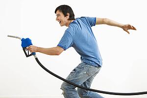 Asian young man aiming gasoline pump nozzle like a gun.