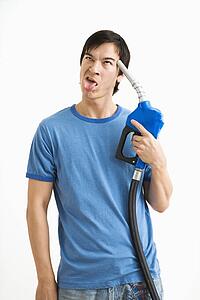 Man holding gasoline pump nozzle to his forehead with disgust on his face