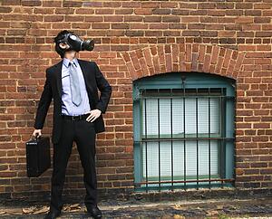 Businessman standing next to brick wall and looking off to side wearing gas mask.