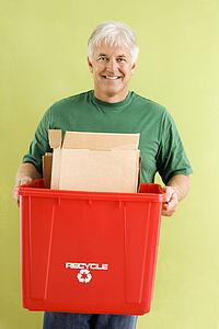 Portrait of smiling adult man holding recycling bin full of cardboard