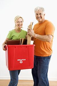 Man and woman smiling while holding recycling bin.
