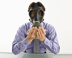 Businessman sitting wearing gas mask holding his hands over his mouth