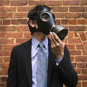 Businessman standing next to brick wall wearing gas mask
