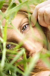Close up portrait of pretty redhead lying in grass looking at viewer.