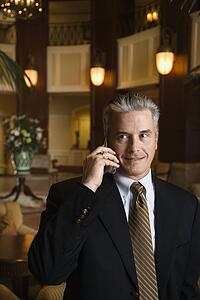 Caucasian prime adult male businessman talking on cellphone in hotel lobby.