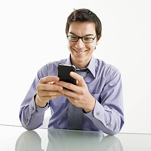 Smiling businessman sitting at desk texting using his pda cellphone