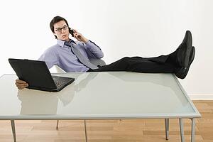 Businessman sitting at desk talking on cellphone and using laptop