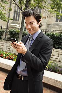 Business man standing looking at cell phone messages smiling