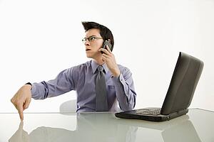 Businessman sitting at desk on cellphone with angry expression
