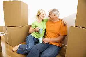 Couple sitting on floor among cardboard moving boxes drinking coffee
