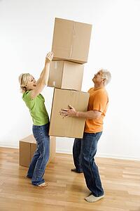 Man holding stack of cardboard moving boxes while woman places another one on
