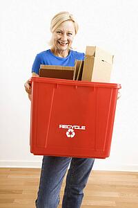 Portrait of smiling adult blonde woman holding recycling bin full of cardboard