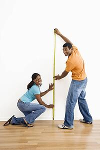 Man and woman measuring wall and looking at viewer