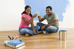 Couple toasting with wine next to half-painted wall and painting supplies
