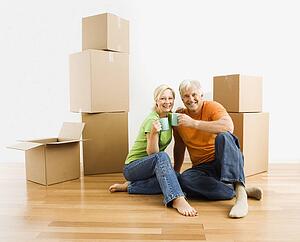 Couple sitting on floor among cardboard moving boxes with coffee