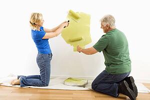 Couple beginning to paint wall green over drop cloth