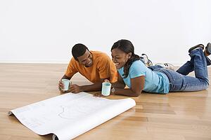 Couple lying on floor looking at architectural blueprints