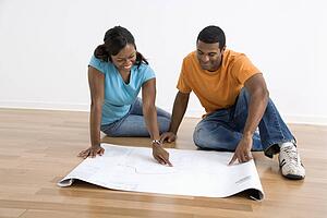 Male and female couple sitting on floor looking at architectural blueprints